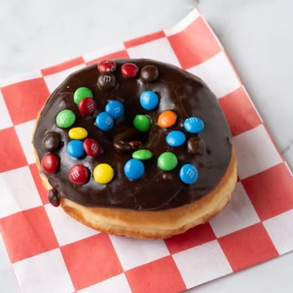 Chocolate frosted donut with colorful M&M's on a red and white checkered napkin.