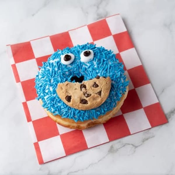 A Cookie Monster themed donut with blue sprinkles, candy eyes, and a chocolate chip cookie mouth.