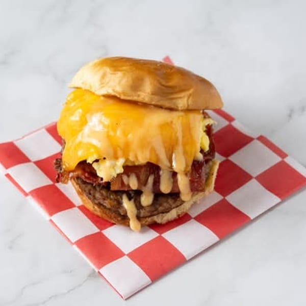 Cheesy breakfast burger with bacon and scrambled eggs on a red and white checkered napkin.