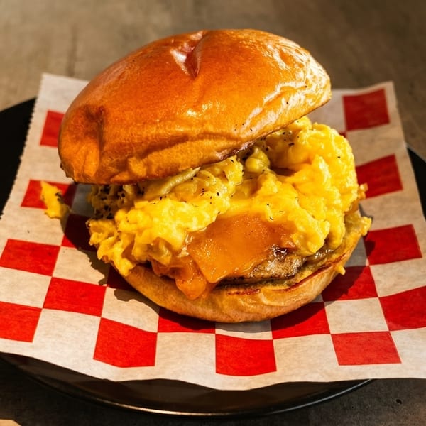 A breakfast sandwich with scrambled eggs, cheese, and a patty on a brioche bun.